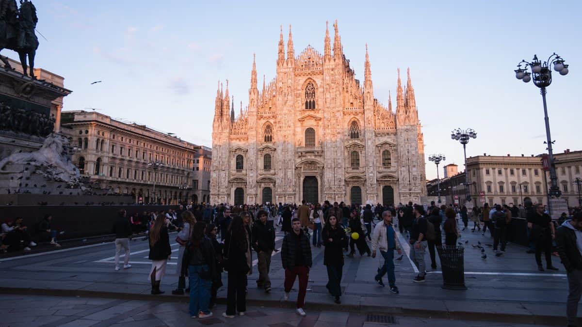 The Duomo di Milano glowing during an orange/pink sunset with crowds of tourists in the square