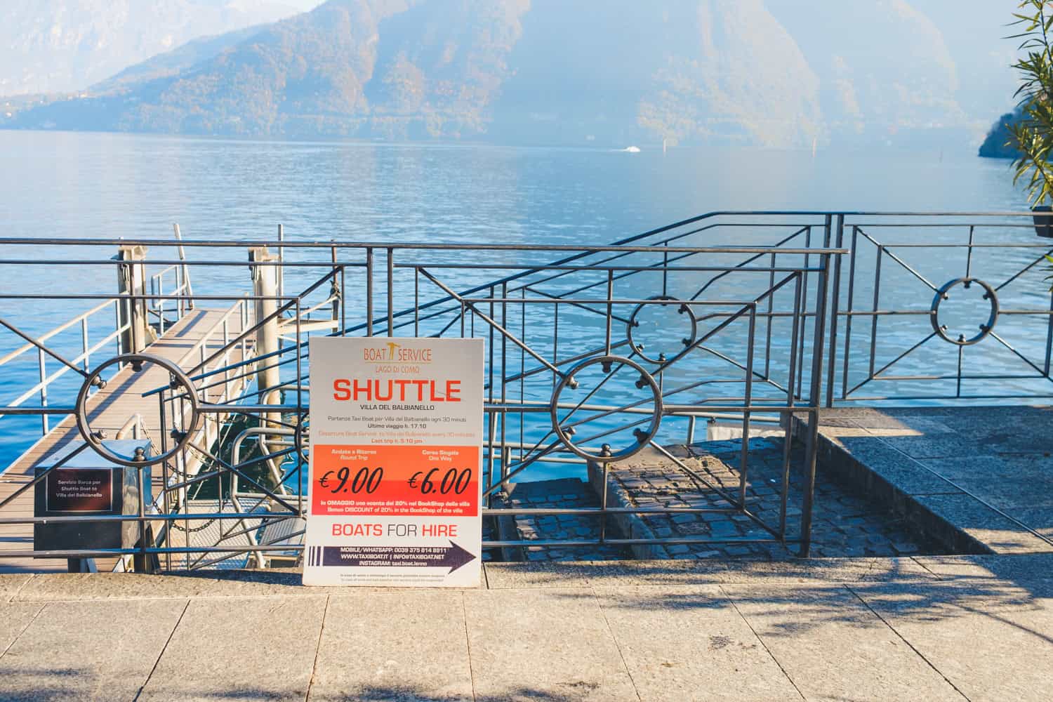 A sign against a railing signaling where the taxi boat for Villa Balbianello leaves from and the ticket prices