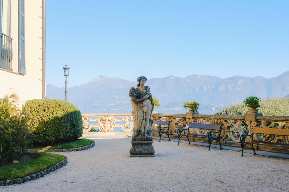 A classic statue of a woman in Villa Balbianello's gardens, surrounded by the park and a few benches on a sunny day