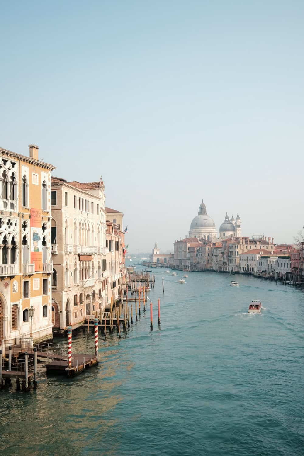 Venice: a view of canale grande from ponte dell'accademia during a sunny day. Gothic palaces line the canal, where many boats are cruising. In the distance there's the big church of Santa maria della salute.