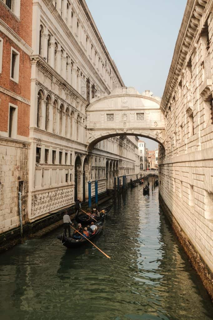 A gondola glides beneath the historic Bridge of Sighs in Venice, Italy, surrounded by the city's iconic architecture.